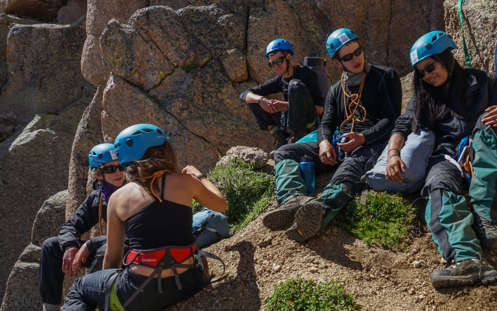 A group of people wearing safety gear rest on rocks.